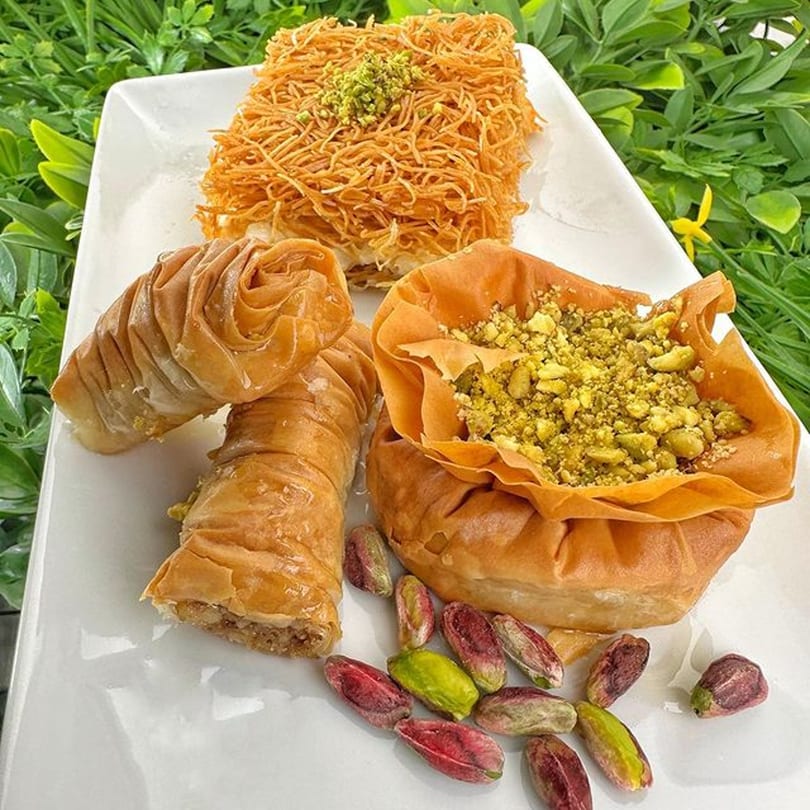 A white plate holds three types of Georgian baklava desserts with scattered pistachios.