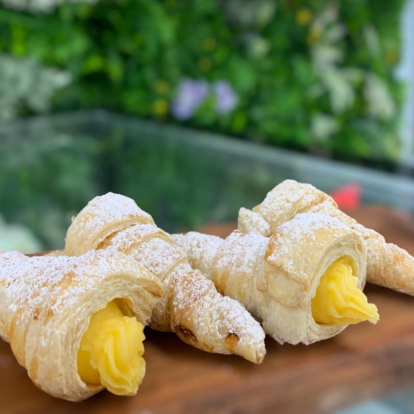 Puff pastry cream horns, dusted with powdered sugar and filled with yellow cream, on a wooden board.