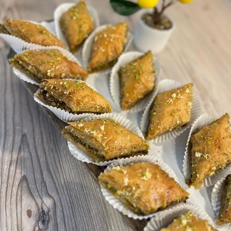 A wooden tray filled with rows of golden-brown baklava pastries, each in a white paper cup.
